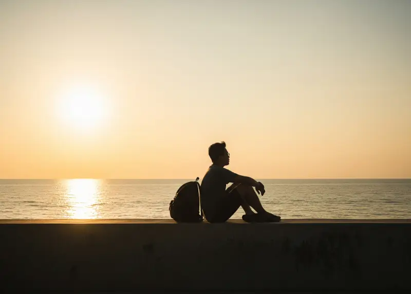 budget travel mindset philippines Filipino backpacker with a small bag watching the sunset by the seawall.