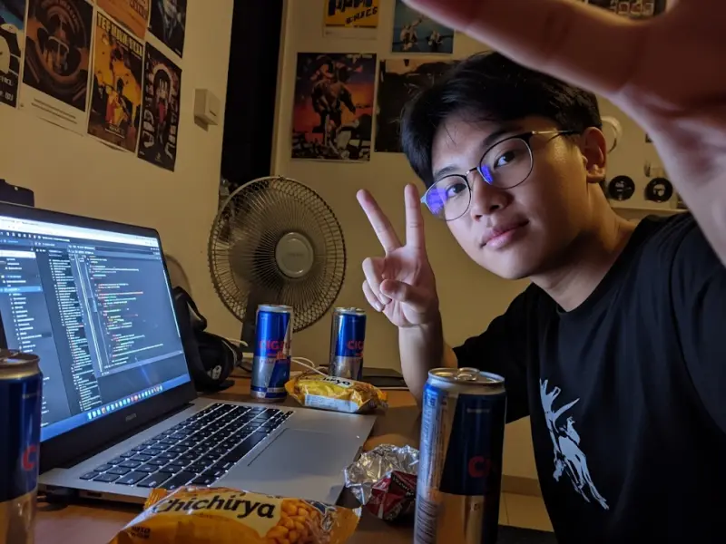 filipino web developer selfie Web developer selfie coding on laptop at night with snacks and fan nearby.